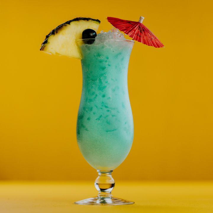 син хавайски коктейл с гарнитура от ананас и чадър, поставен на жълт фон