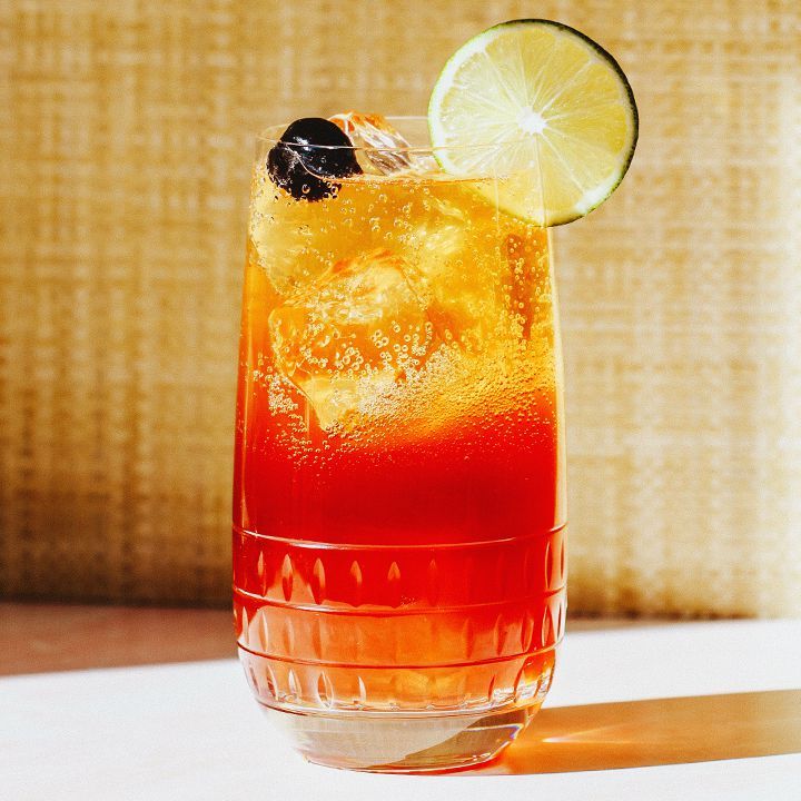 Cocktail Cherry Bomb dans un verre highball avec garnitures de citron vert et de cerises
