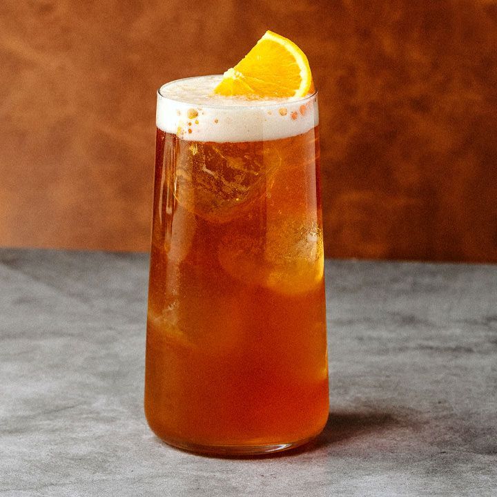 Un verre Collins rempli d'un cocktail de bière brun rougeâtre, garni d'une demi-roue orange sur une tête de mousse