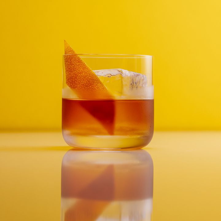 Rum Old Fashioned kokteil apelsinikoore garneeringuga, mida serveeritakse kollasel taustal