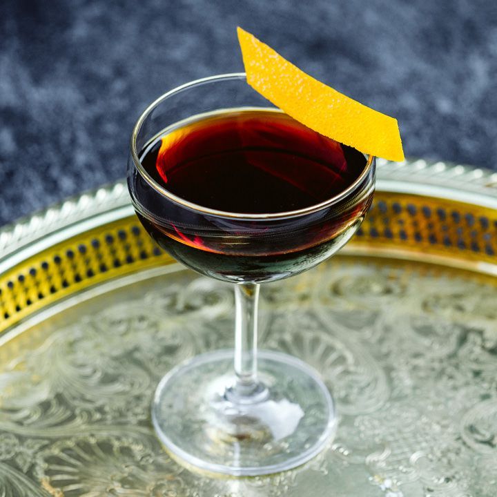 Downhill marrom escuro Coquetel ousado em um copo cupê com casca de laranja na borda, servido em uma bandeja redonda de metal