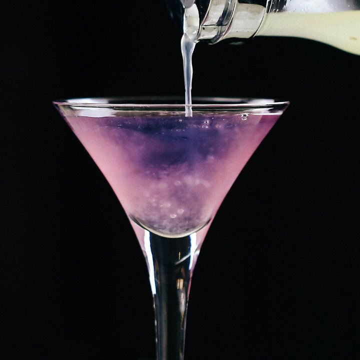Citroensap wordt in de kleurveranderende martini gegoten, waardoor deze van paars naar roze verandert