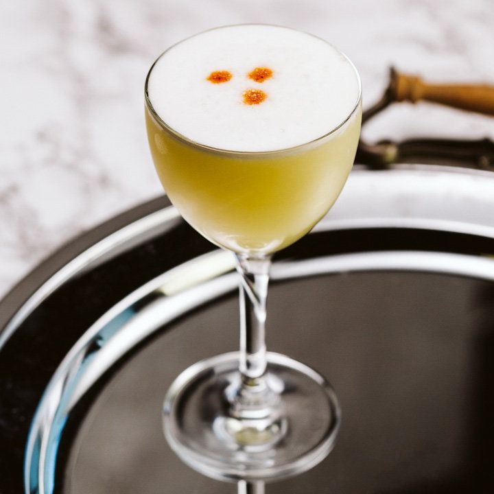 cocktail pisco sour avec trois gouttes d'amer sur le dessus, servi sur un plateau en argent